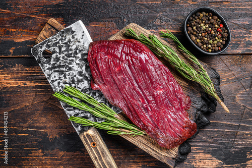 Venison raw meat steak on a cuuting board with rosemary. Black background. Top view photo