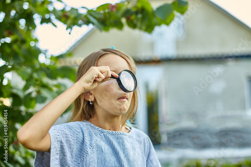 Little girl playing with a magnifying glass in her backyard make faces