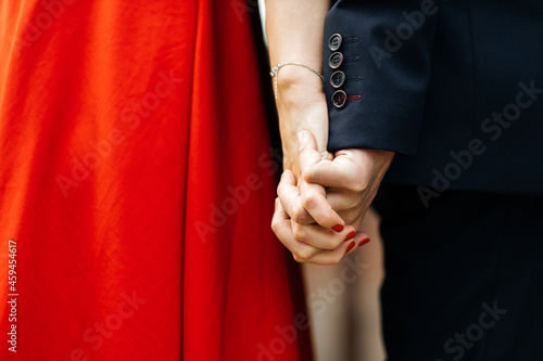 Close-up of the hands of a man and a woman. A romantic couple holds each other's hands. Family holiday. A red dress.
