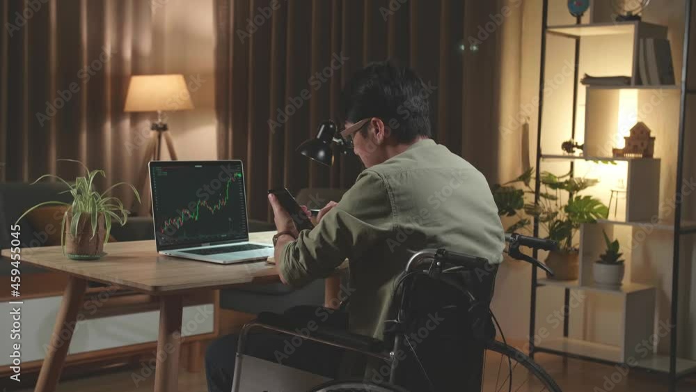Asian Man Trader Investor Sitting In A Wheelchair Using Mobile Phone App Analytics For Cryptocurrency Financial Market Analysis, Trading Data Index Chart Graph On Smartphone And Laptop Screen. Back Vi Asian Man Trader Investor Sitting In A Wheelchair Using Mobile Phone App Analytics For Cryptocurrency Financial Market Analysis, Trading Data Index Chart Graph On Smartphone And Laptop Screen. Back Vi