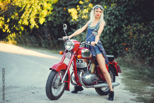 The biker is a beautiful cheerful girl sitting on her motorcycle, a little crazy. Wear short shorts and glasses. holding the steering wheel the wind blows the hair. Looks into the distance at the road