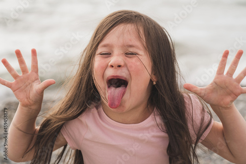 The child indulges and pranks. A little girl shows her tongue. Funny girl writhes her face. Little girl wants to become an actress