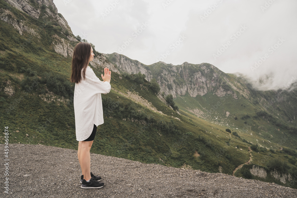 A girl meditates in the mountains. Yoga Retreat in Nature. A girl in a white shirt enjoys the beautiful nature. The girl sits in the lotus position with her eyes closed.