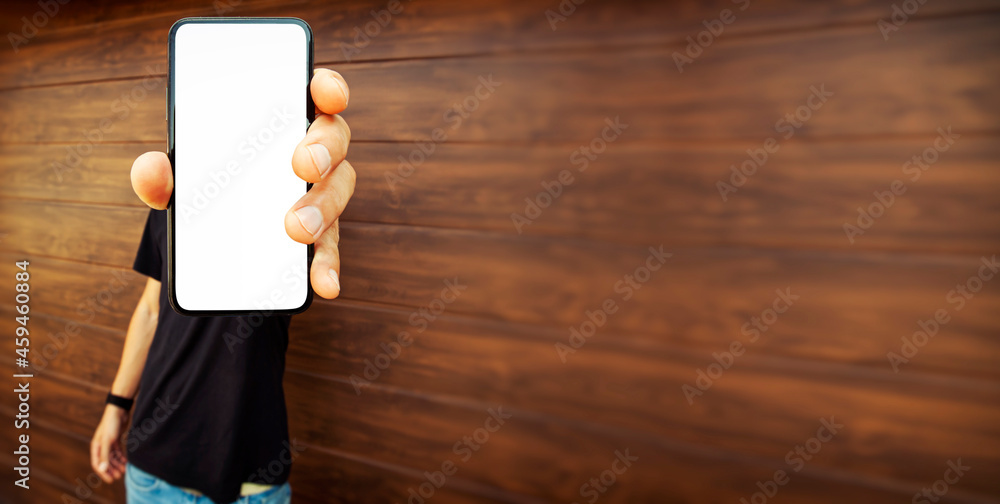 Guy holds mobile phone with blank screen near brown wall Guy holds mobile phone with blank screen near brown wall