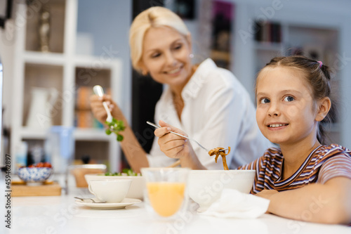 White mother and daughter smiling while having lunch in kitchen at home