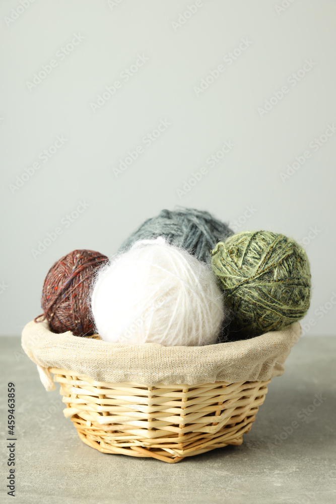 Fototapeta premium Wicker basket with yarn balls on light gray table