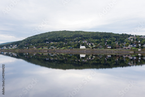 Beautiful symmetric landscape featuring the Wakeham road and a small Anglican church reflected in the South-West Basin, Gaspé, Quebec, Canada