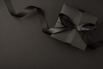 Top view photo of black gift box with black ribbon bow on isolated black background with empty space