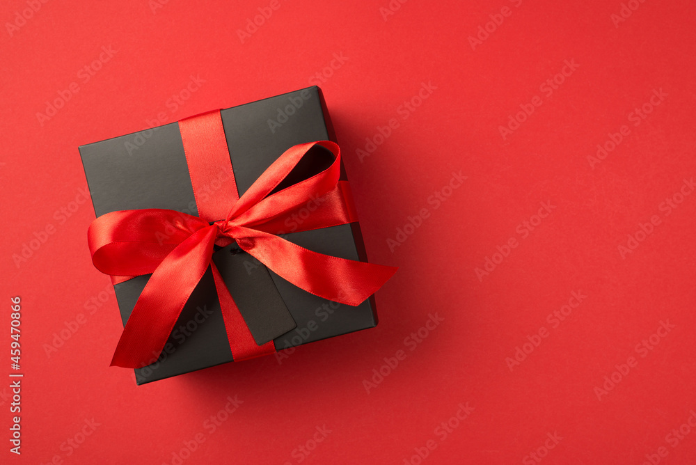 Top view photo of black giftbox with red ribbon bow and tag on isolated red background with blank space Top view photo of black giftbox with red ribbon bow and tag on isolated red background with blank space