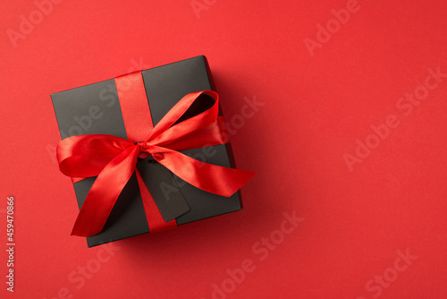 Top view photo of black giftbox with red ribbon bow and tag on isolated red background with blank space