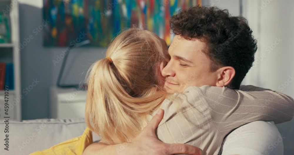 A pretty blonde sits on the couch next to her fianc , hugs him longingly, throws herself on his neck, embraces tightly, expresses pride, satisfaction, praises boyfriend, congratulates A pretty blonde sits on the couch next to her fianc , hugs him longingly, throws herself on his neck, embraces tightly, expresses pride, satisfaction, praises boyfriend, congratulates