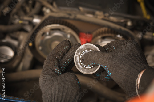 An auto mechanic checks the condition of the timing belt tensioner roller of a passenger car photo