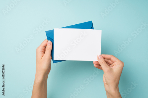 Fototapeta Naklejka Na Ścianę i Meble -  First person top view photo of hands holding blue envelope and white card on isolated pastel blue background with empty space