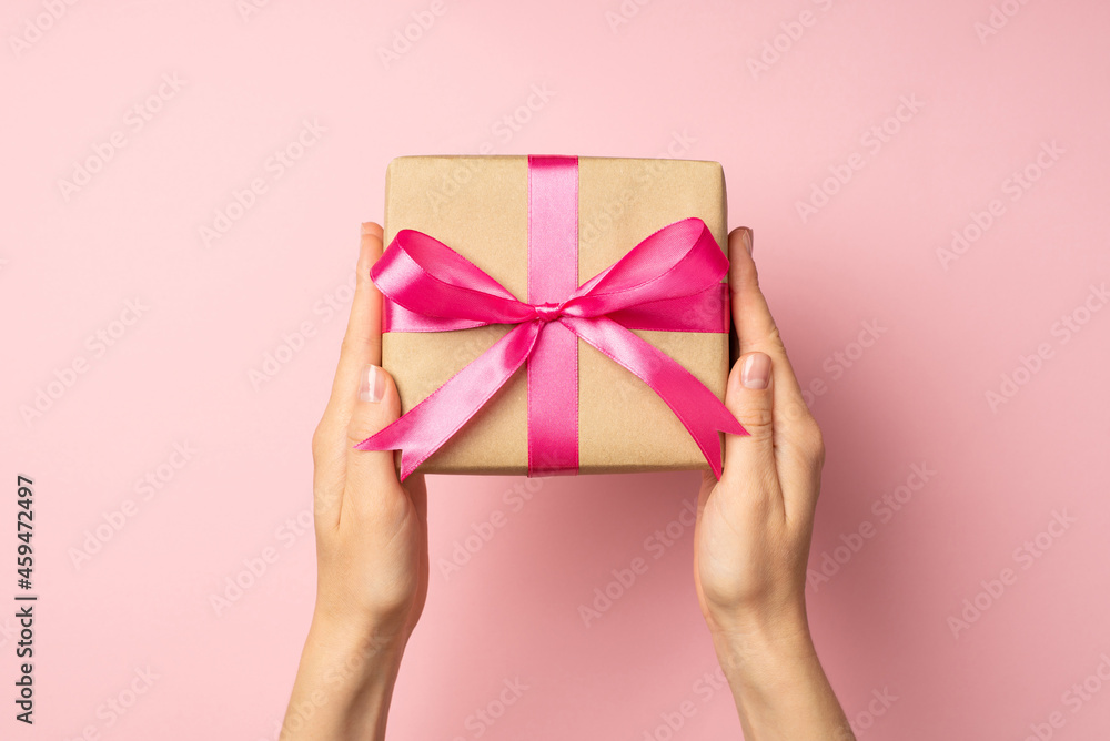 First person top view photo of hands holding stylish craft paper giftbox with pink ribbon bow on isolated pastel pink background First person top view photo of hands holding stylish craft paper giftbox with pink ribbon bow on isolated pastel pink background