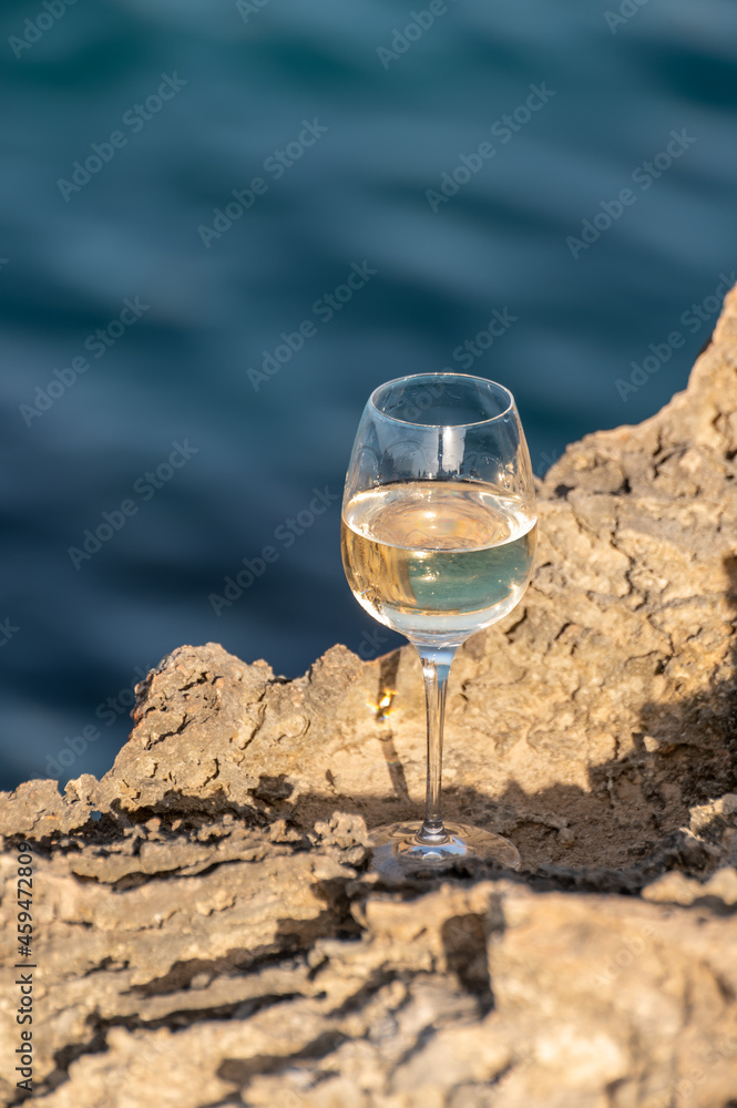 Glass of cold white dry white wine served on rocks in blue sea bay near Protaras touristic town on Cyprus