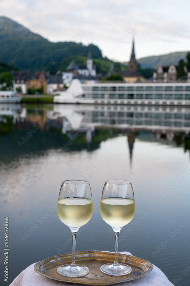 Obraz premium Tasting of white quality riesling wine served on outdoor terrace in Mosel wine region with Mosel river and old German town on background, Germany