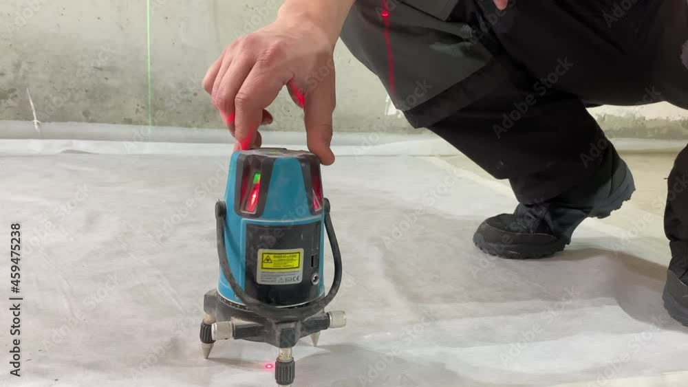 Worker turning on laser level device cement floor measuring markers