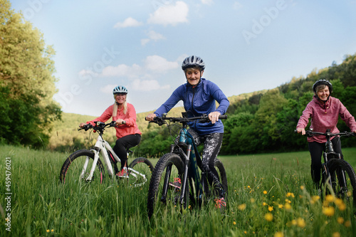 Low angle view of happy active senior women friends cycling together outdoors in nature.