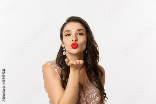 Concept of New Year celebration and winter holidays. Close-up of sensual young woman in dress, pucker lips and blowing air kiss at camera, white background
