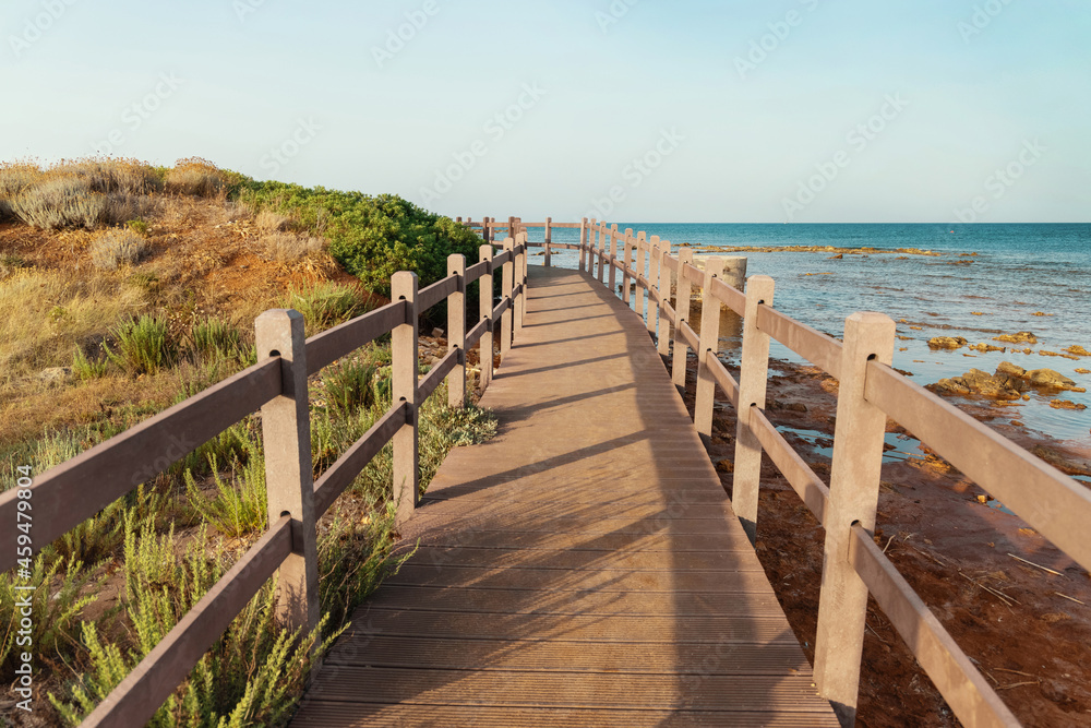 Beautiful peaceful landscape with wooden pier, grass covered hill, calm sea and blue sky