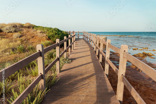 Beautiful peaceful landscape with wooden pier  grass covered hill  calm sea and blue sky