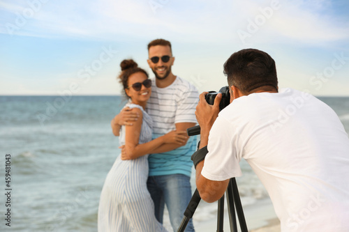 Photographer taking picture of couple with professional camera near sea © New Africa