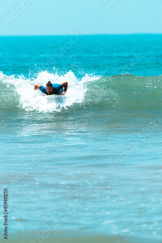 Surfer mężczyzna łapiący falę na desce na tle niebieskiego oceanu i błękitnego nieba.