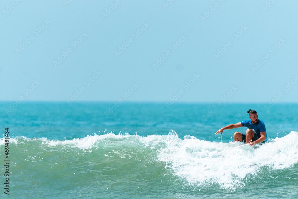 Surfer mężczyzna łapiący falę na desce na tle niebieskiego oceanu i błękitnego nieba.