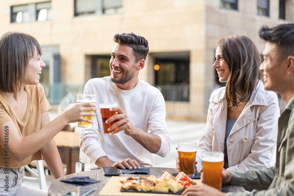 Happy friends drinking beer at the outdoor pub in the city - Friendship lifestyle concept with young millennial people enjoying time together at open air pub