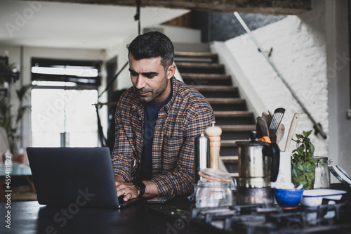 Mid adult hispanic male using laptop in kitchen photo