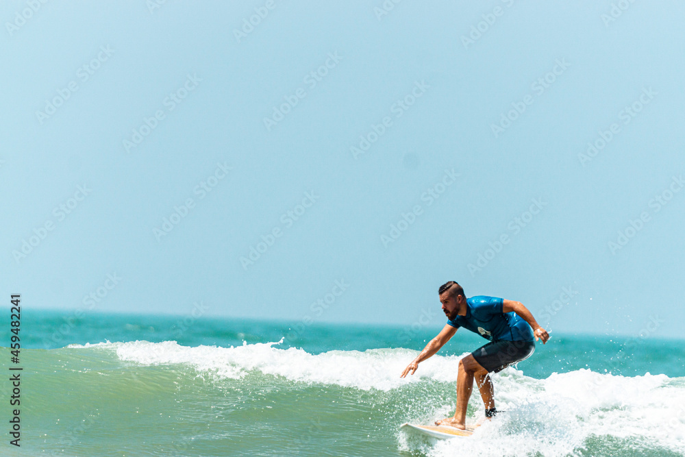 Mężczyzna surfer płynący na fali na tle błękitnego oceanu i nieba. - obrazy, fototapety, plakaty 