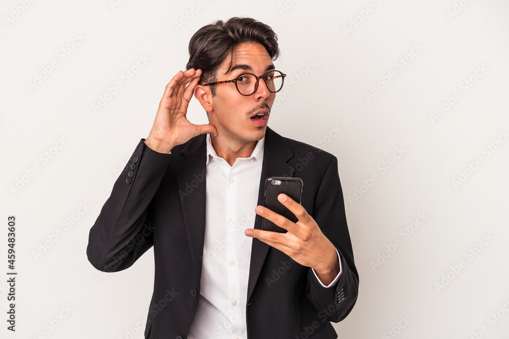 Young mixed race business man holding mobile phone isolated on white background trying to listening a gossip. Young mixed race business man holding mobile phone isolated on white background trying to listening a gossip.