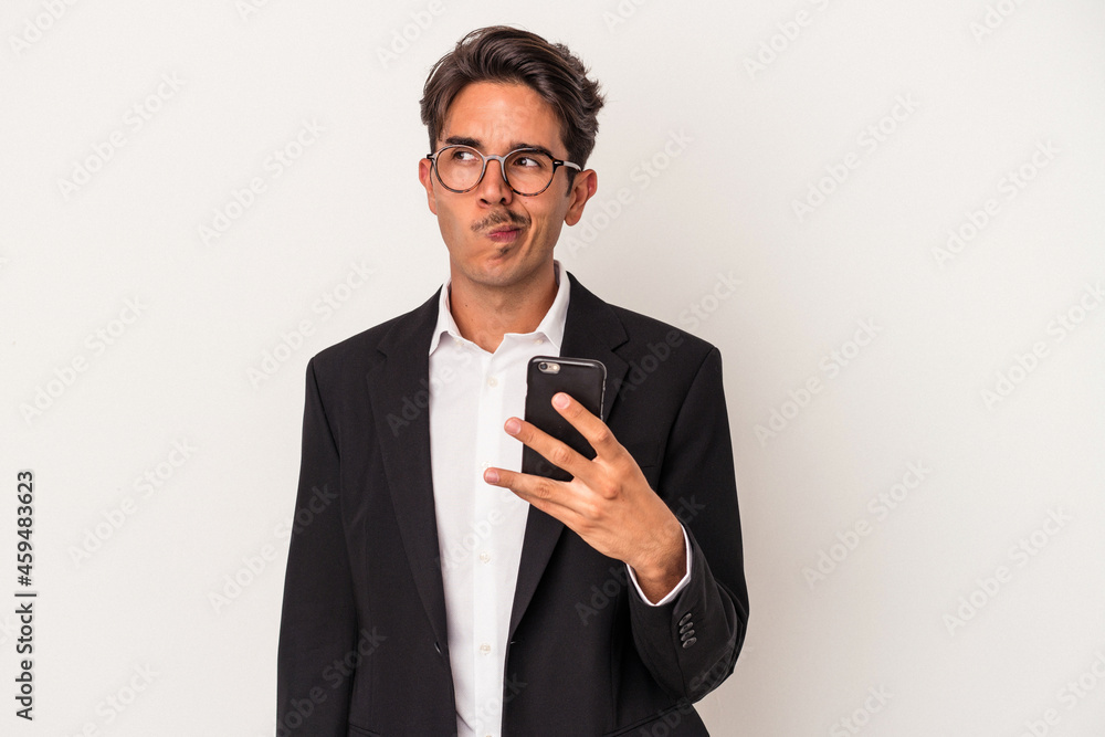 Young mixed race business man holding mobile phone isolated on white background confused, feels doubtful and unsure. Young mixed race business man holding mobile phone isolated on white background confused, feels doubtful and unsure.