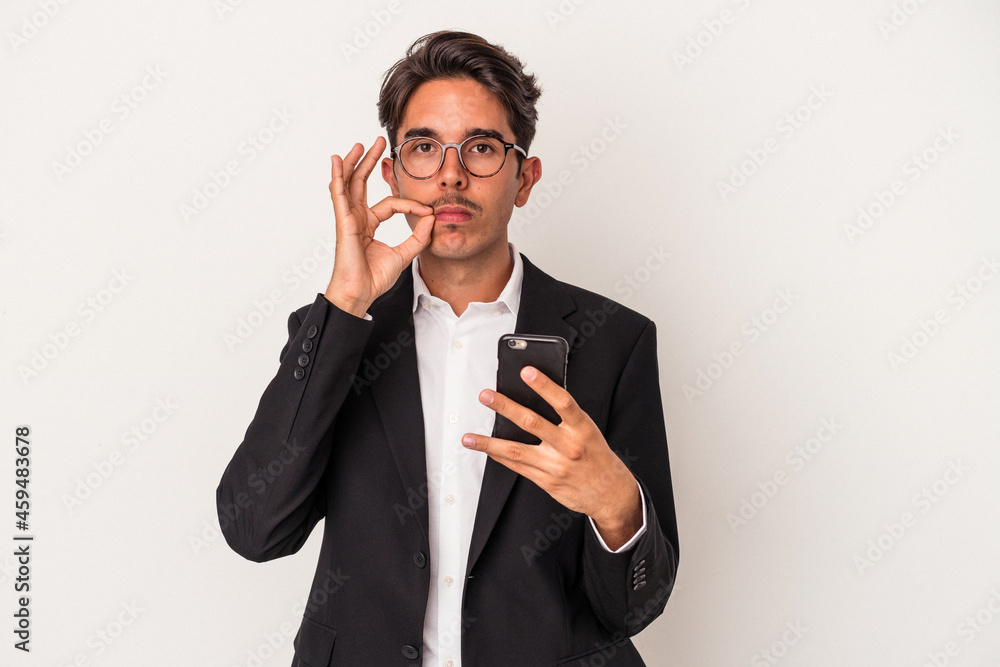 Young mixed race business man holding mobile phone isolated on white background with fingers on lips keeping a secret. Young mixed race business man holding mobile phone isolated on white background with fingers on lips keeping a secret.