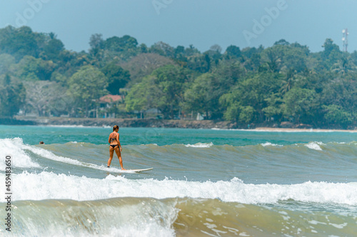 Dziewczyna surfująca na fali, na tle oceanu i wybrzeża.