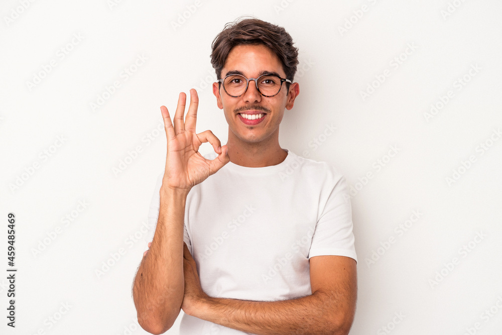 Young mixed race man isolated on white background winks an eye and holds an okay gesture with hand. Young mixed race man isolated on white background winks an eye and holds an okay gesture with hand.