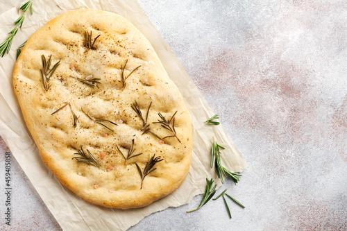 Foto Freshly baked Italian traditional homemade focaccia bread baking with seasonings and rosemary on parchment paper and light gray background