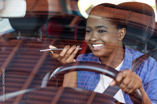 Close-up of woman using mobile phone and talking on the speaker while driving car. A shot of a African American female in her 20's sitting in her car talking on her phone using her speakerphone.