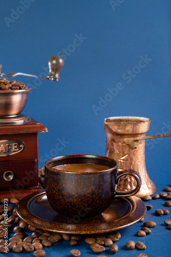 Cup with coffee, copper turk and manual coffee grinder with coffee beans on a blue background. Photo