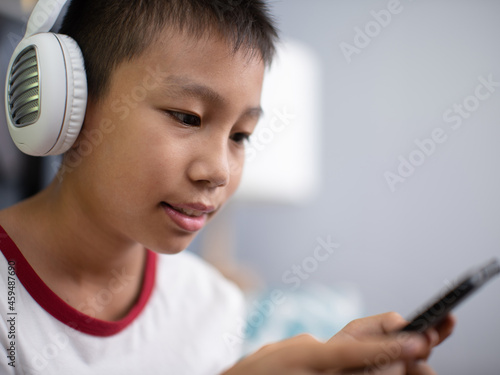Asian boy wearing headphones and holding a phone.