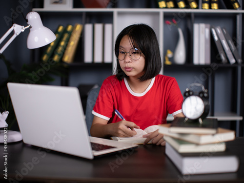 Smart asian girl child sit at table study at laptop make notes write in notebook, schoolgirl handwrite prepare homework assignment, prepare task at home, distant education concept
