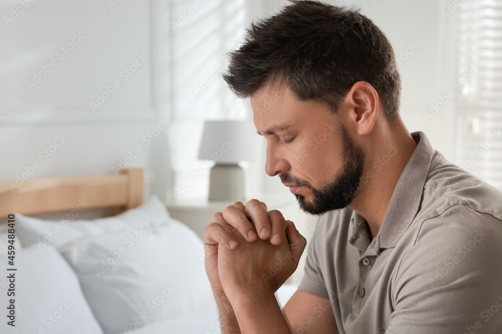 Religious man praying in bedroom. Space for text
