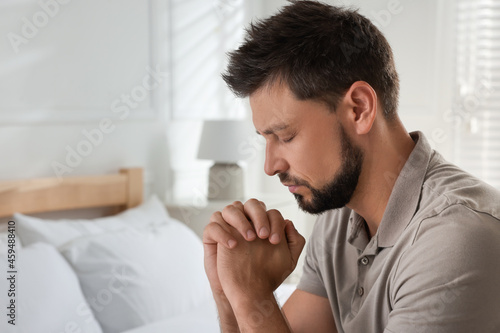 Religious man praying in bedroom. Space for text