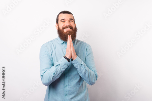Bearded man holding hands together is praying hopefully for a miracle over white background.