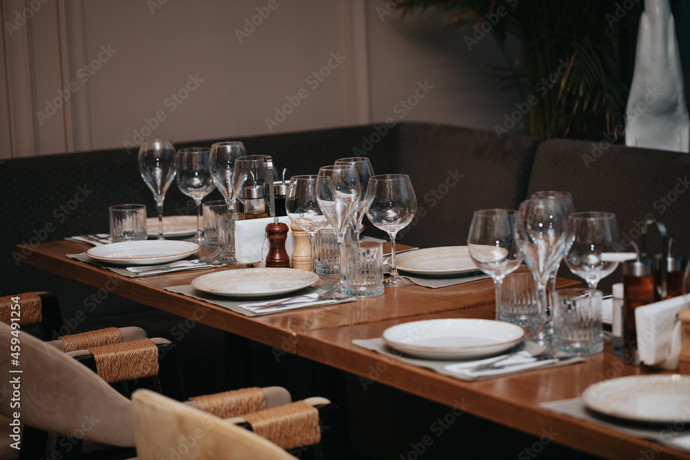 Beautiful table set in elegant restaurant with glass of wine, glass of water, knife, spoon and fork, cutlery, ready to welcome customers.
