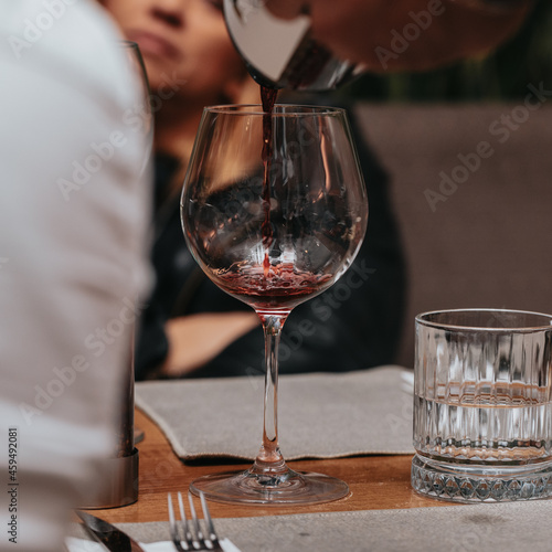 Elegant waiter pours red wine from bottle into glass at restaurant. Sommelier tasting wine in restaurant. Copy space for text menu elegant or recipe on dark background.