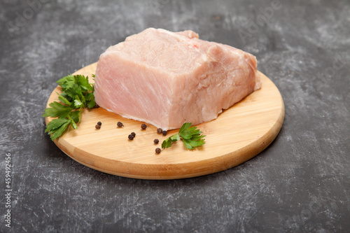 A piece of raw meat with herbs lies on a wooden cutting board on a black background.