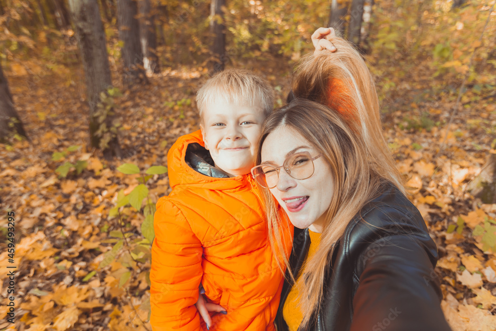 Son and mother are taking selfie and having fun in autumn park. Single parent, leisure and fall season concept. Son and mother are taking selfie and having fun in autumn park. Single parent, leisure and fall season concept.