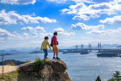瀬戸大橋・瀬戸内海を眺める兄弟　岡山県倉敷市　Asian boys standing on the rock and watching the view of Setonaikai, Inland Sea of Japan, and Seto Ohashi bridge in Kurashiki city, Okayama pref. Japan.