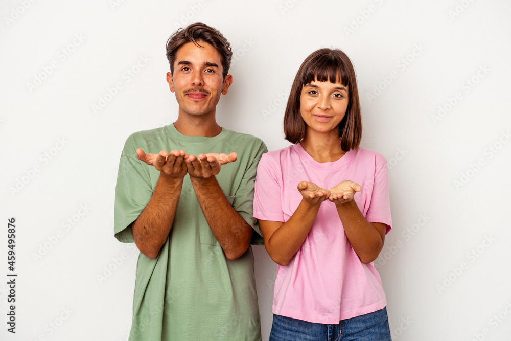Young mixed race couple isolated on white background holding something with palms, offering to camera. Young mixed race couple isolated on white background holding something with palms, offering to camera.